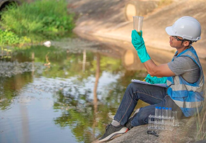 Young male collecting water sample in a test tube for analysis and studies.